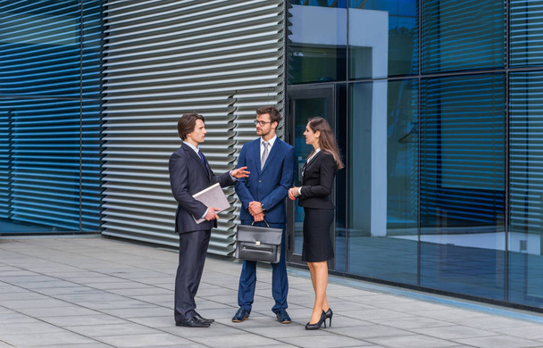 Confident businesspersons talking in front of modern office building. Businessmen and businesswoman have business conversation. Banking, professional job and financial market concept. - Valokuva, kuva
