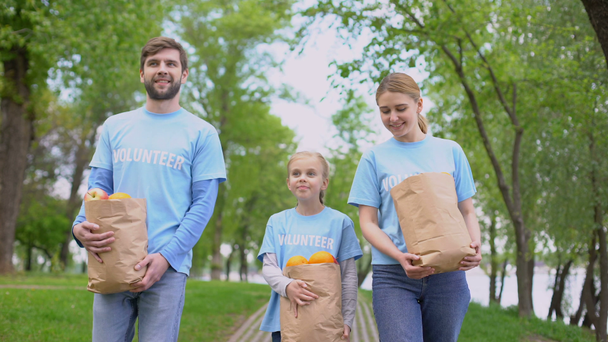 Volunteers family walking park holding paper bags with apples and oranges, help - Séquence, vidéo