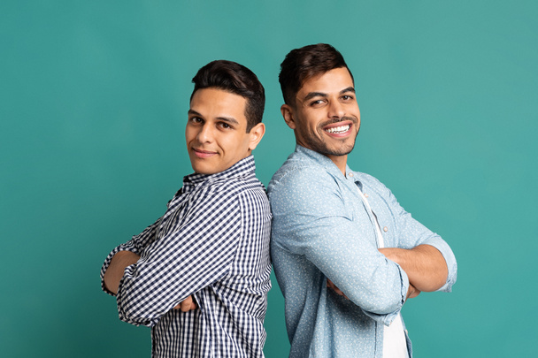 Два латиноамериканских парня, стоящих спиной к спине на бирюзовой студии
 - Фото, изображение