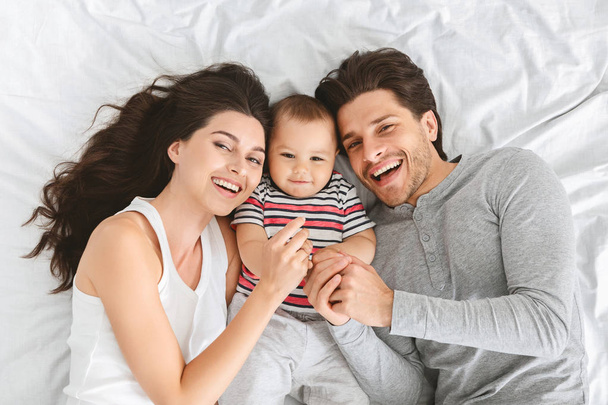 Cheerful mom and dad embracing with cute baby in bed - Foto, imagen