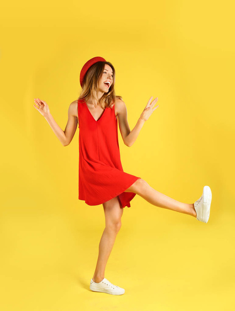 Szép fiatal nő piros ruhában táncoló sárga háttér - Fotó, kép