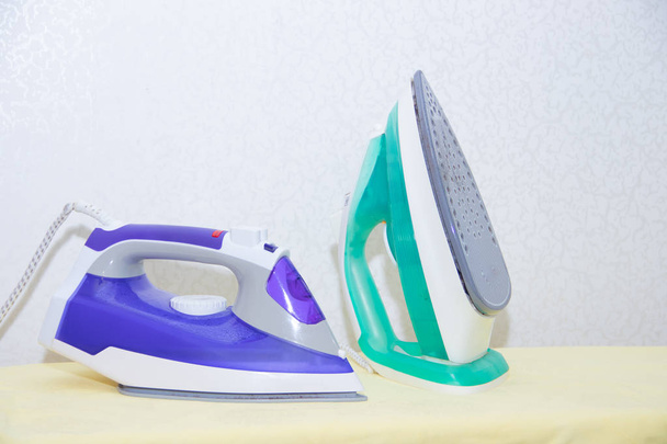 Two irons on an ironing board. Selection and comparison of irons. Ironing board. - Photo, image