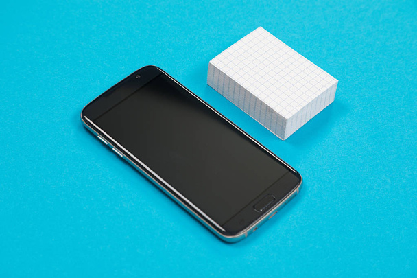 Черный мобильный телефон и куча белой чешуйчатой бумаги лежат на лазурной поверхности изолированы
 - Фото, изображение