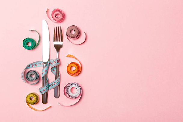 Composition of fork and knife surrounded with colored balled measuring tapes on pink background. Top view of obesity concept with copy space - Foto, Imagen
