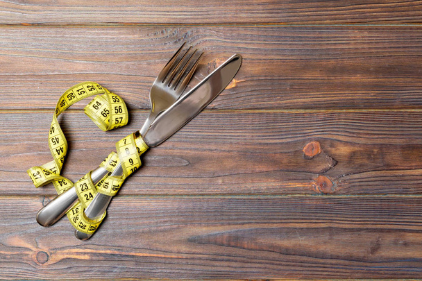 Diéta és egészséges étkezési koncepció keresztbe villával és késsel és mérőszalag fa háttér. Felülnézet a Weightloss - Fotó, kép