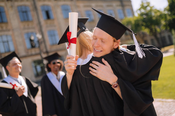 Dos graduados abrazándose frente a su universidad
. - Foto, Imagen