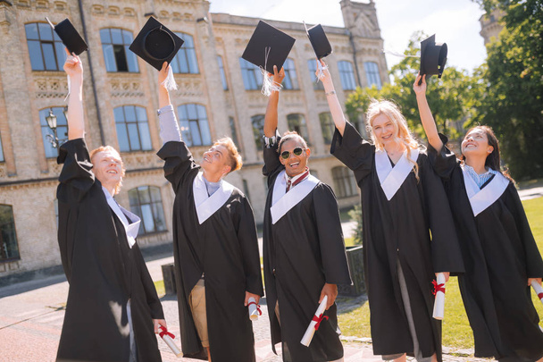 Cheerful graduates raising their masters caps in the air. - Photo, Image