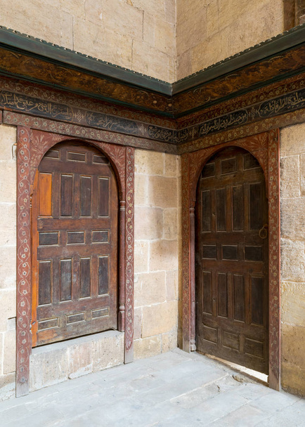 Две деревянные украшенные сводчатые перпендикулярные двери на каменных кирпичных стенах
 - Фото, изображение