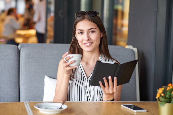 Young business woman in a cafe reading an ebook and drinking coffee - Foto, imagen