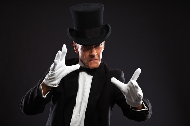 Mágico a fazer gestos misteriosos. Vestindo terno preto e chapéu
. - Foto, Imagem