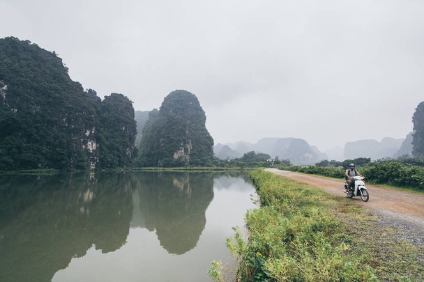 Ninh Binh eyaletinde kireçtaşı dağları arasında motosiklet sürme Adam, Vietnam. - Fotoğraf, Görsel