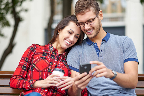 Happy couple with smart phone. Happy young loving couple standing outdoors together and looking at the mobile phone together - Foto, Imagen