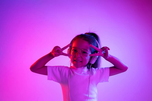 Portrait of little girl in headphones on purple gradient background in neon light - Фото, зображення