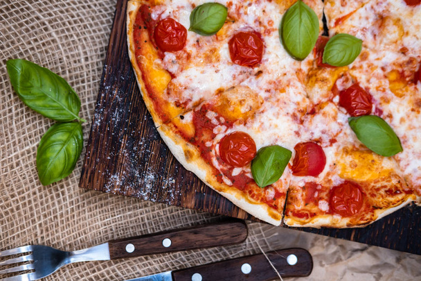 Margarita pizza on wooden board with cutlery and basil leafs  - Photo, Image