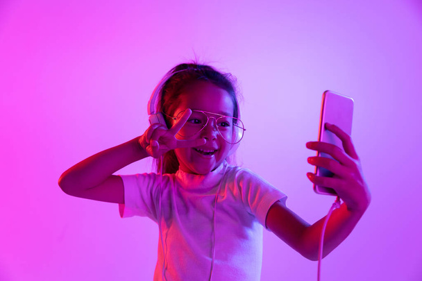 Portrait of little girl in headphones on purple gradient background in neon light - Foto, imagen