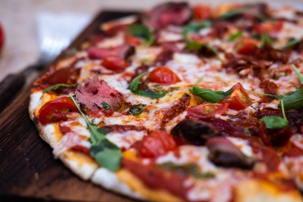 Pizza with beef slices, tomato sauce and some greens. Pizza is on wooden board. Close up view  - Foto, afbeelding