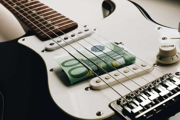 Money under the strings of a guitar. One hundred euros under the strings of a guitar. - Photo, Image