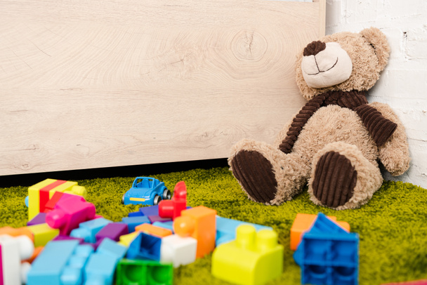 Plush bear and scattered pieces of construction on green carpet - Foto, imagen