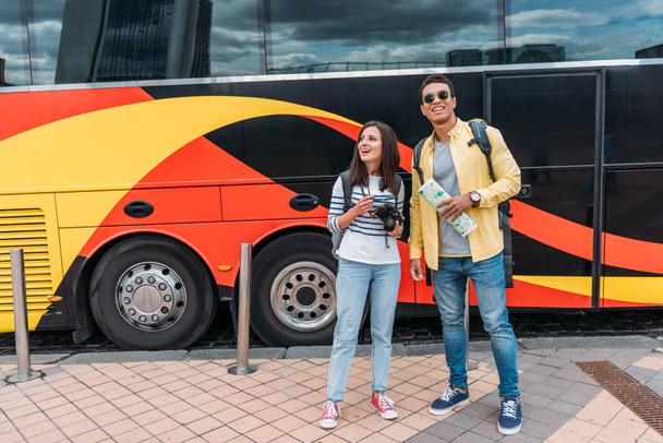 Mixed race man with map and woman with digital camera near travel bus - Photo, Image