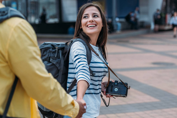 Woman with digital camera and backpack holding hand of friend  - Fotografie, Obrázek