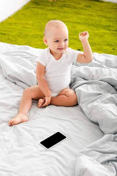 Criança adorável sentada na cama perto do dispositivo digital e levantando a mão
 - Foto, Imagem