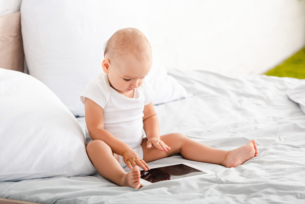 Cute barefoot child in white clothes pointing with fingers at digital tablet  - Foto, Imagem