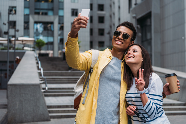 Bi-racial man in sunglasses with woman taking selfie on smartphone - Фото, зображення