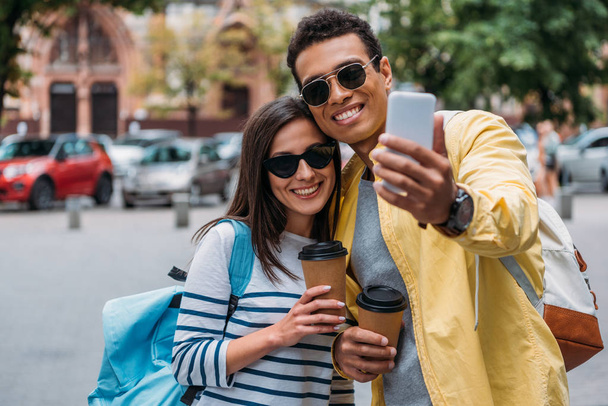 Bi-racial man taking selfie with woman holding paper cup - 写真・画像