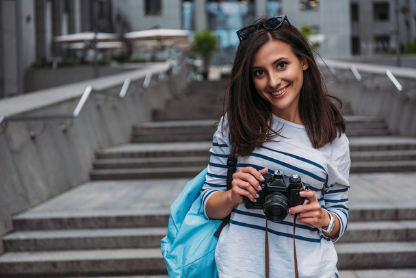 Woman in casual with backpack holding digital camera and smiling - Foto, Imagem