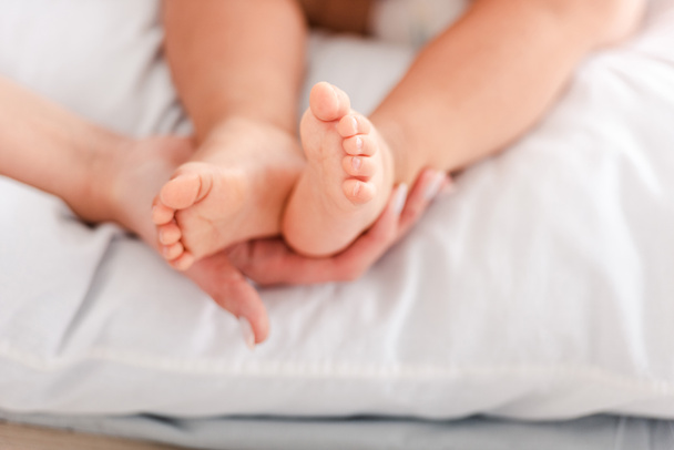 小さな裸足の赤ちゃんの足に触れる母親のトリミングされたビュー - 写真・画像