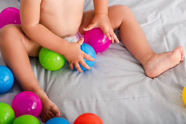 Cropped view of cute little baby on bed grabbing colored balls with tiny hands - Foto, imagen