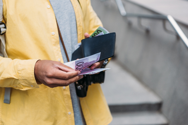 vista recortada del hombre de raza mixta que sostiene la cartera mientras cuenta los billetes en euros
  - Foto, Imagen