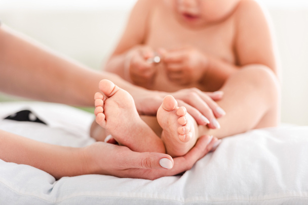 Cropped view of mother touching feet on little daughter - Photo, Image