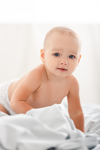 Cute little child crawling on white fabric and looking at camera - Photo, Image