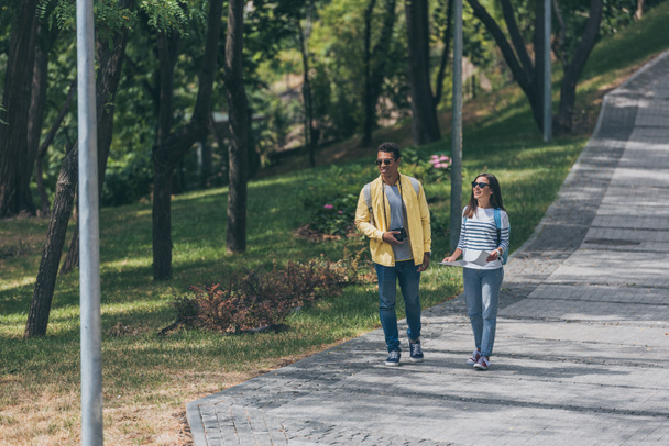 happy mixed race man and attractive woman walking in park  - 写真・画像