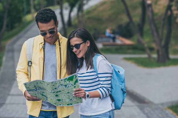 happy mixed race man in sunglasses and cheerful girl looking at map  - Fotografie, Obrázek