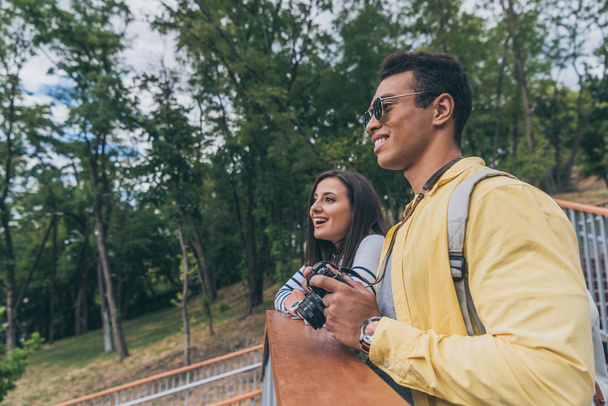 счастливый смешанной расы мужчина держит цифровую камеру рядом веселая девушка в парке
  - Фото, изображение