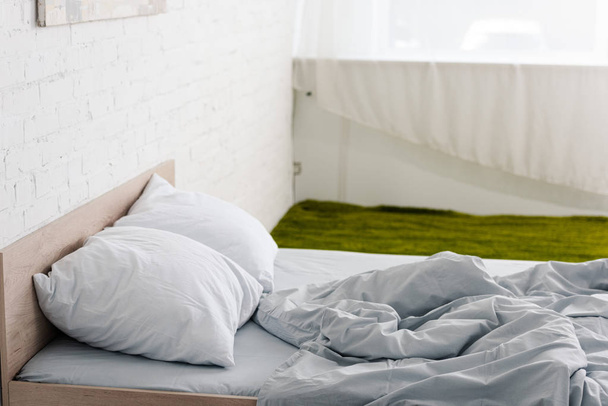 Yeşil halı ile beyaz odada yastık ve buruşuk Hafif battaniye ile ahşap yatak - Fotoğraf, Görsel