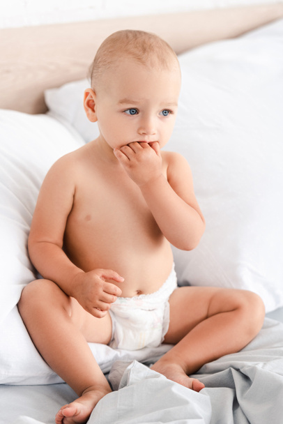 Urocze małe dziecko siedzi na łóżku z miękkimi białymi poduszkami - Zdjęcie, obraz