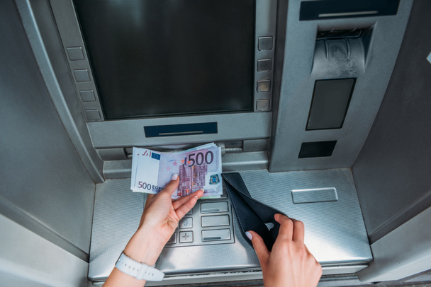 vue de dessus de la femme tenant l'argent et le portefeuille noir près de la machine d'ATM
  - Photo, image