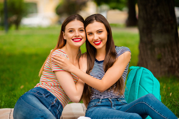 Portrait of sweet girls with red lips-stick cuddling wearing striped t-shirt denim jeans sitting on plaid blanket in town - Zdjęcie, obraz