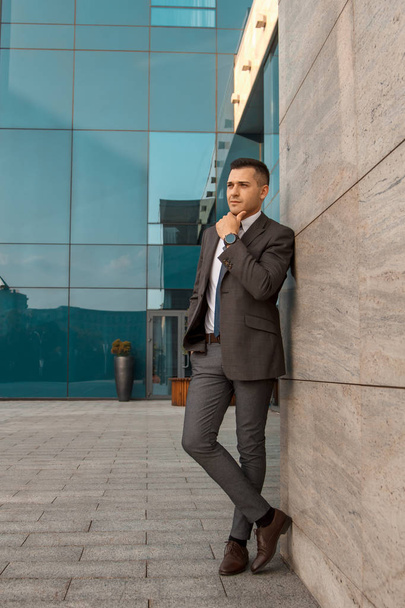 Business concept. Male business portrait. Young man in a suit near a business building. A man looks into the distance and waits for someone - Fotoğraf, Görsel