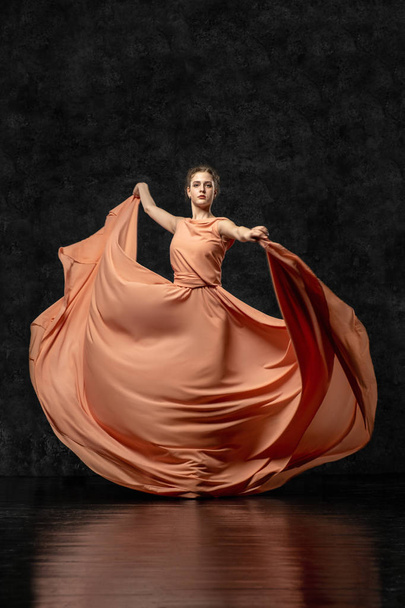Ballerina. A young dancer dressed in a long peach dress, pointe shoes with ribbons. Performs a graceful, graceful dance movement. Beautiful classic ballet. Advertising ballet studio. Volumetric photos - Фото, изображение