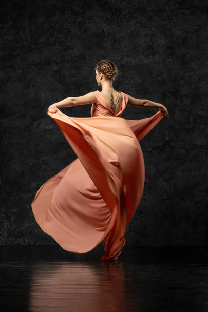 Ballerina. A young dancer dressed in a long peach dress, pointe shoes with ribbons. Performs a graceful, graceful dance movement  which is visible from the back. Beautiful classic ballet.  - Foto, Imagem