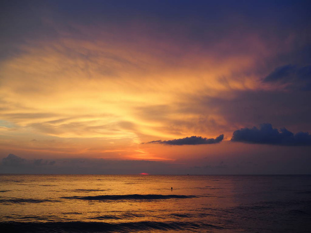 Punainen auringonlasku meren yllä, runsaasti tummia pilviä, valonsäteitä - Valokuva, kuva