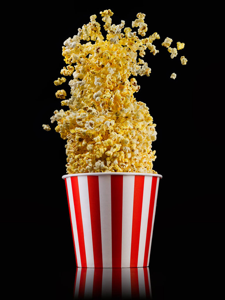 Flying popcorn from striped bucket isolated on black background - Foto, imagen
