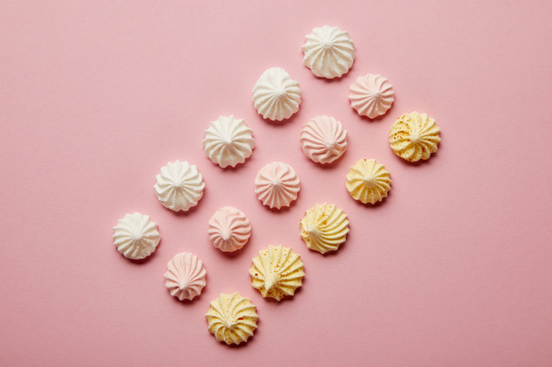 Vista superior de merengues brancos, rosa e amarelos em fileiras no fundo rosa
 - Foto, Imagem
