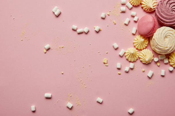 Κορυφαία θέα από γλυκά ροζ μακαρόνια, μαρέγκες και ζαχαρωτά με κίτρινα κομμάτια σε ροζ φόντο - Φωτογραφία, εικόνα