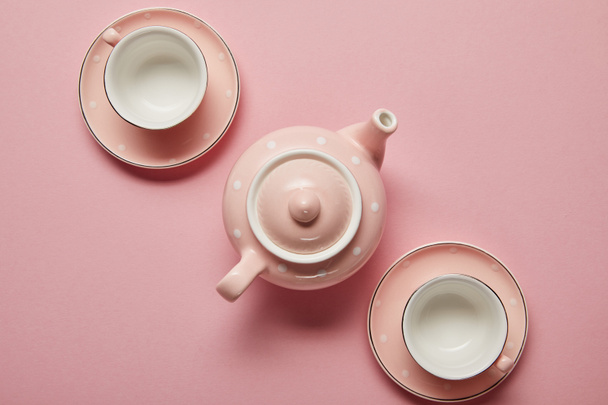 Pastel roze gestippelde theepot en kopjes met schoteltjes op roze achtergrond - Foto, afbeelding