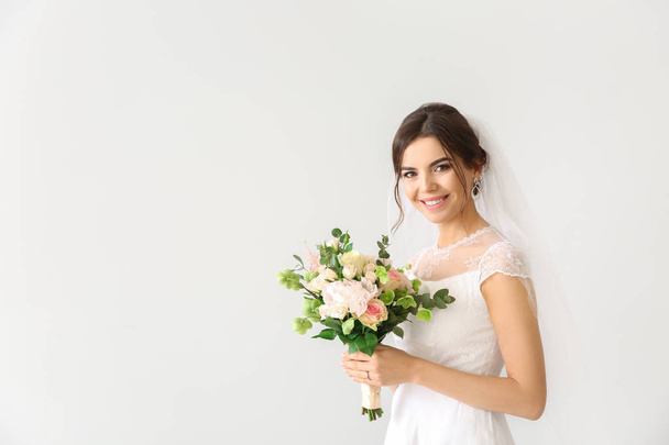 Beautiful young bride with bouquet of flowers on light background - Photo, Image